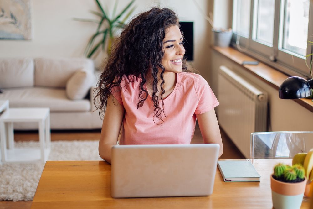 Lachende vrouw bij een laptop in een thuiskantoor, symbool van tevredenheid en welzijn dankzij aromatherapie tijdens het werk